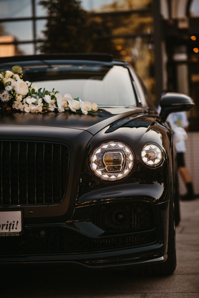 A dark wedding car dressed with a white floral arrangement
