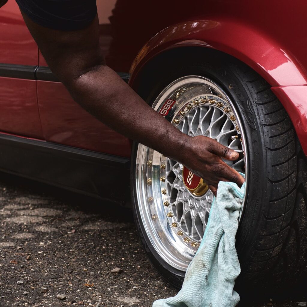 A hand cleaning the wheel of a red car